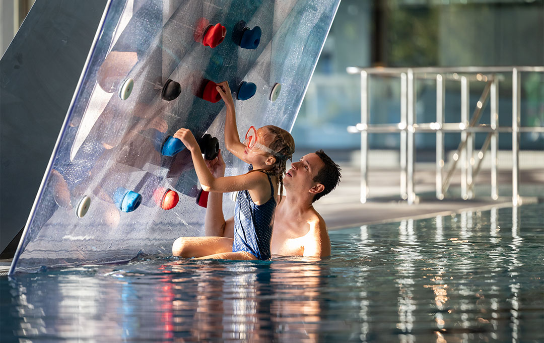 Vater hilft Tochter beim klettern an der Kletterwand im Sportbecken