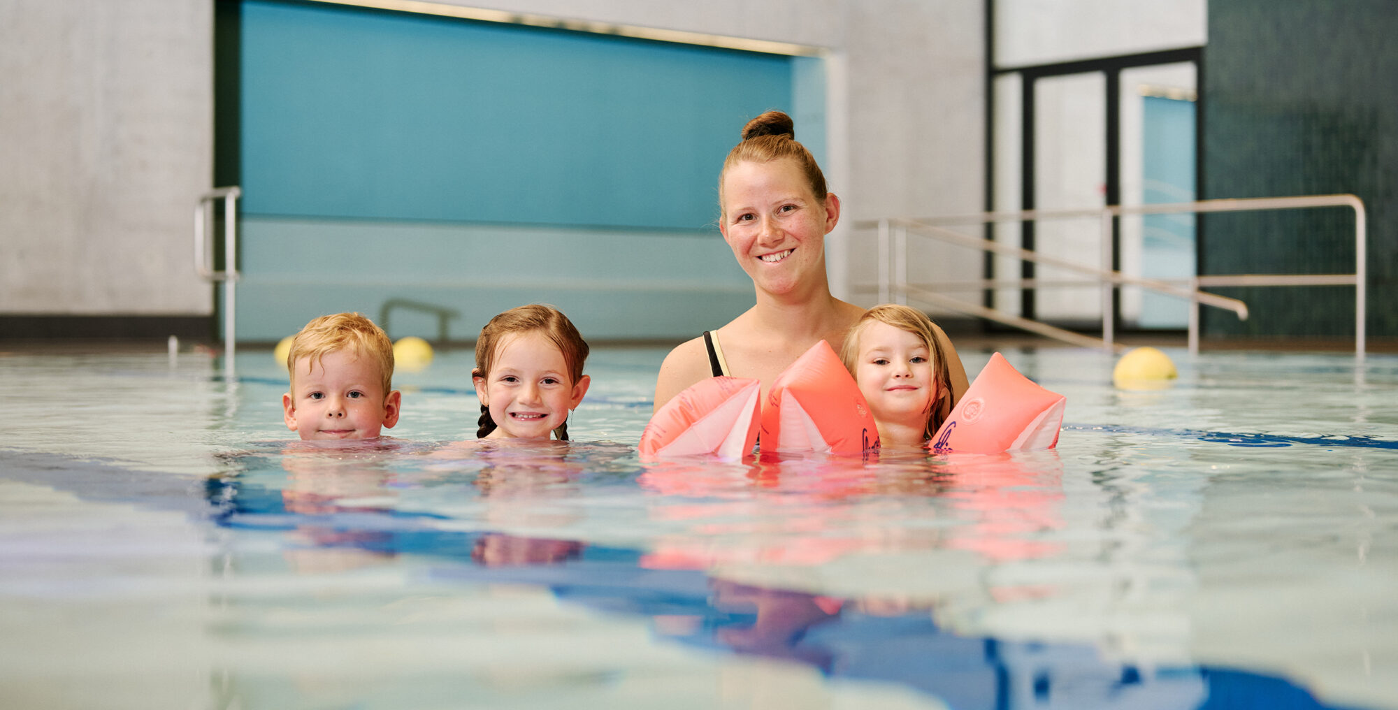 Kursleiterin mit zwei Mädchen und einem Jungen, mit Schwimmflügeln